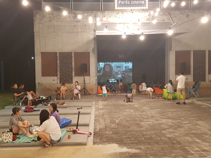 야외와 실내가 연결된 숲속에서 영화를 즐기고 있는 시민들 