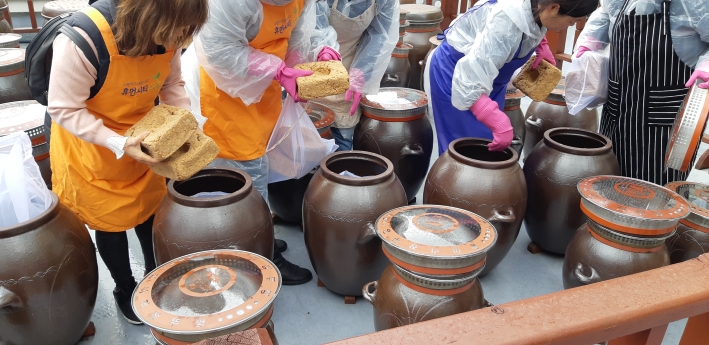 수원시청 옥상 장독대에서 진행된 '전통 저염장 담그기' 체험 교육에서 시민들이 메주를 항아리에 담고 있다.