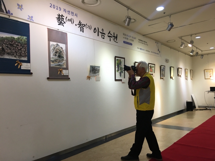    2019년 노인 재능나눔활동 지원사업 '기타활동' 활동인 최모 씨가 한 전시관에서 사진촬영을 하면서 취재하고 있다. 