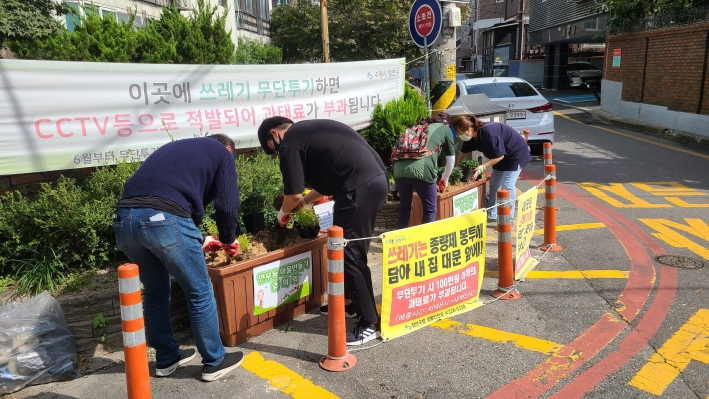 연무동 마을만들기협의회 회원과 자원봉사자들이 설치한 대형 꽃 화분에 국화와 황금조팝을 심고 있다.