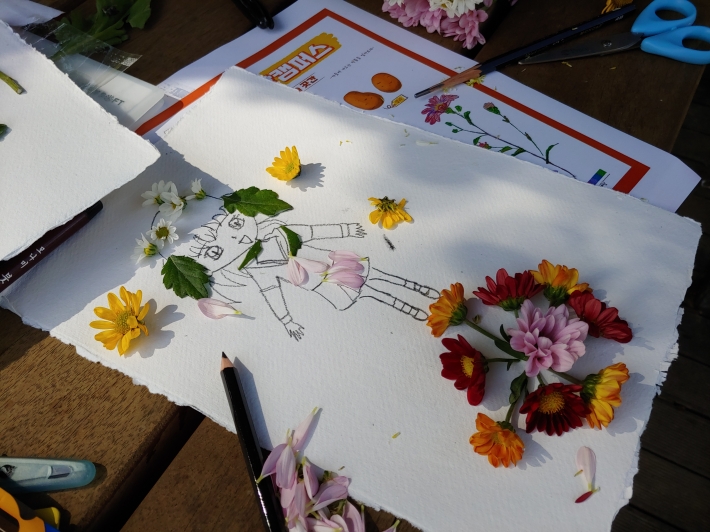 아이들이 그림 위에 국화꽃으로 장식을 하고 있다. 