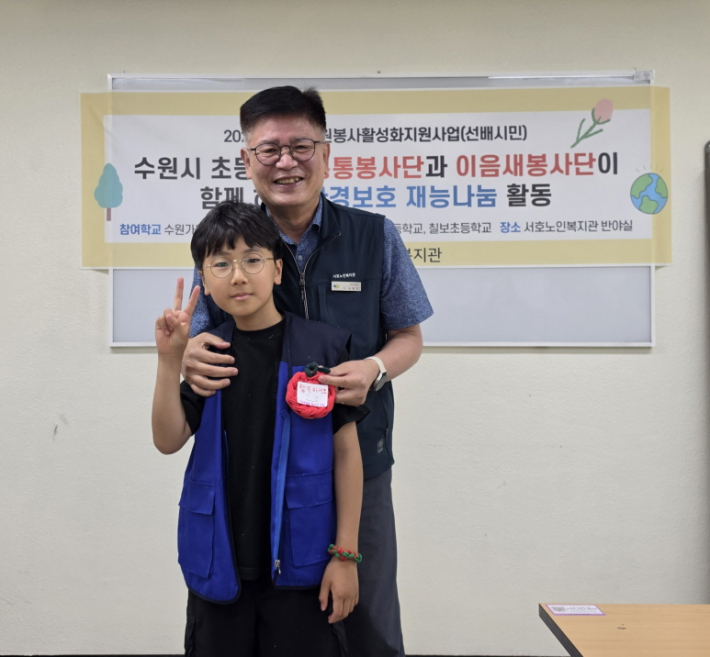수원중촌초 봉사단원이 노인복지관 관장님께 컵받침을 전달하고 사진을 촬영하고 있다.