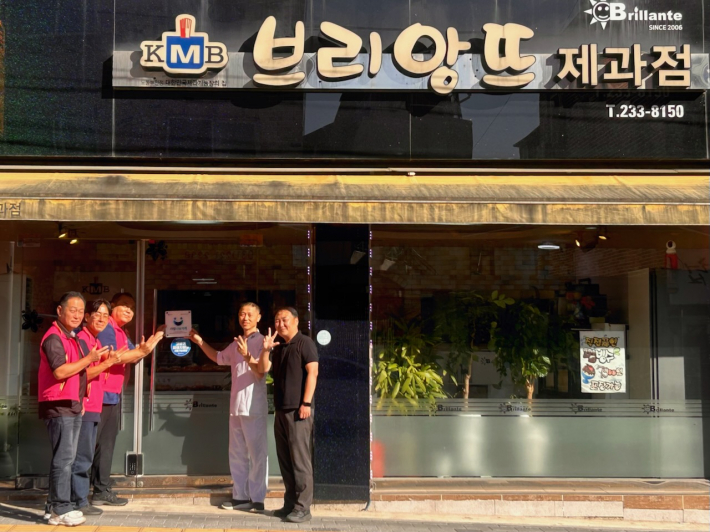 세류3동 지역사회보장협의체가 브리앙뜨과자점에 「사랑나눔가게」 현판을 전달하고 기념촬영을 하고 있다.