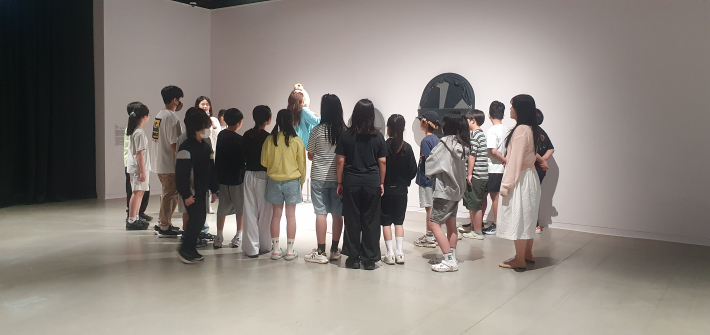 어린이 관람객들이 《패트리샤 피치니니: 킨쉽》 전시장에서 작품 설명을 들으며 전시를 살펴보고 있다.