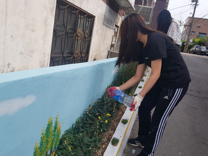 더운 날씨로 인해 꽃이 시든 마을화단에 물을 주고 있는 에코가이드 학생들.