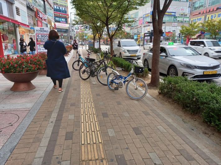 자전거 주차장이 보행 도로 바닥에 그림으로 표시되어 있고, 거치대가 따로 없다. 이로 인해 자전거 주차가 무질서하고, 사람들의 보행을 막고 있다.  