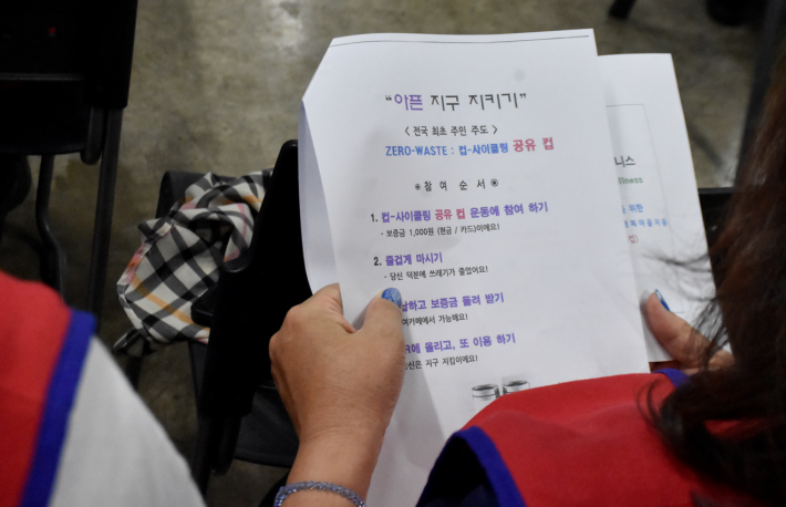 컵-사이클링 공유 컵 사용을 위한 안내지를 살피고 있는 참가자