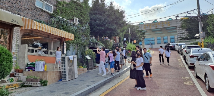 관광객들이 드라마 촬영지 '우영우 김밥'을 배경으로 인증샷하는 장면