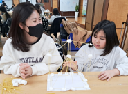 엄마와 아이가 함께 '스파게티로 건축물 만들기' 수업에 참여하고 있습니다.