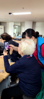 수원대학교 공공정책대학원 자원봉사자가 경로당 어르신에게 스마트폰 사용법을 알려주고 있다. 