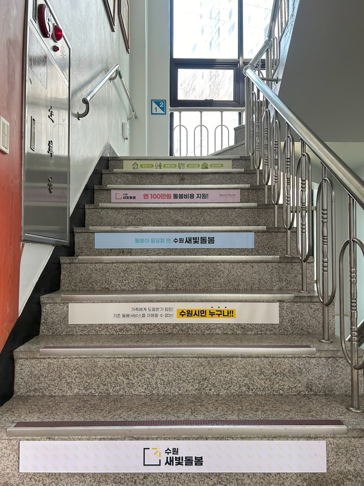 우만2동 행정복지센터는 계단띠를 부착하여 수원새빛돌봄 사업을 홍보하고 있다.