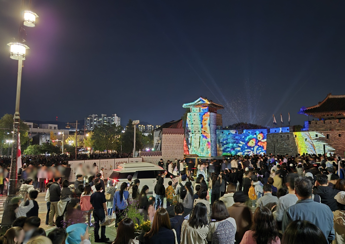 성곽 벽을 화려하게 수놓은 빛의 축제를 관람하고 있는 사람들