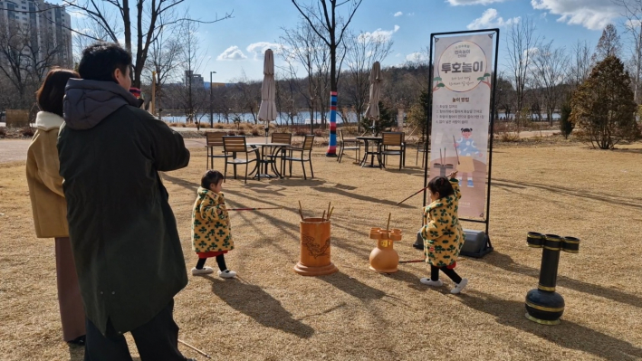 두 쌍둥이가 투호 넣기를 하고 있는 것을 보고 있는 엄마 아빠