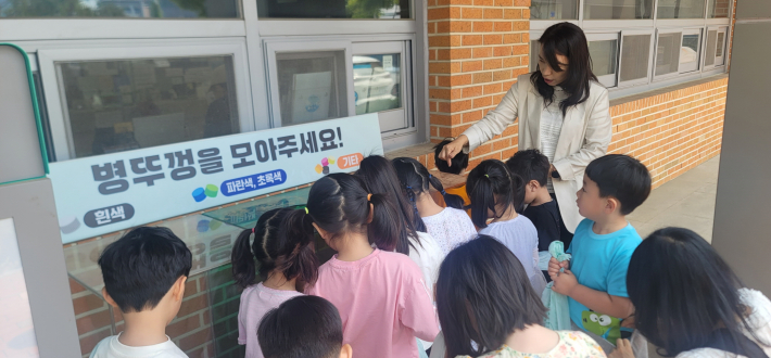 폐 병뚜껑을 활용한 자원의 새활용 설명을 듣고 있다