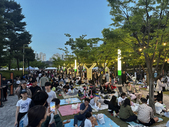만석 공원 나무 그늘 아래, 가족 단위 시민들이 돗자리를 펴고 여유롭게 피크닉을 즐기며 축제의 분위기를 만끽하고 있다.