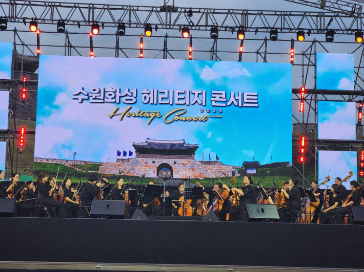 오케스트라 연주자들이 연주를 준비하는 장면. 전통과 현대가 조화를 이루는 무대 디자인과 전면 연출자들의 모습이 콘서트의 품격을 더한다. 