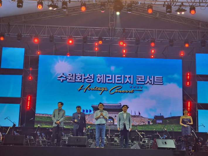 무대 위에 오른 수원시장과 함께 주요 인사들이 나란히 서서 인사말을 전하고 있다. 