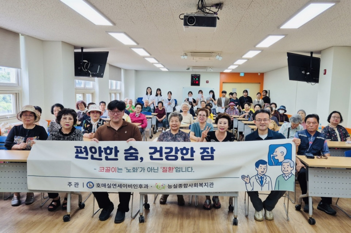 능실종합사회복지관 2층 강당에서 진행한 수면교육에 참여한 주민들과 호매실연세이비인후과 이유재원장, 마이메딕스 공경보대표가 '편안한 숨, 건강한 잠' 문구가 적힌 현수막과 함께 단체사진을 찍었다.