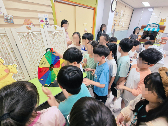 책도장을 모두 찍은 아이가 친구들의 응원을 받으며 룰렛돌리기를 하는 모습