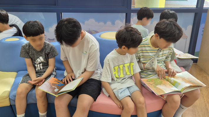 2학년과 5학년이 도서관에서 짝을 지어 책을 읽어주고 있다.