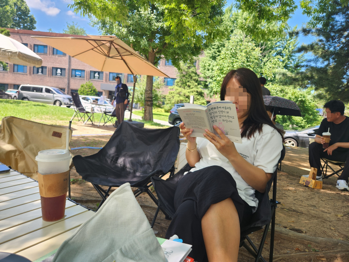 캠핑의자에 앉아 책을 읽고 있는 시민의 모습