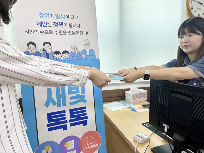 수원시 장안구 정자3동 민생회복 소비쿠폰 접수 창구 직원이 신청자에게 선불카드와 볼펜을 주고 있다.