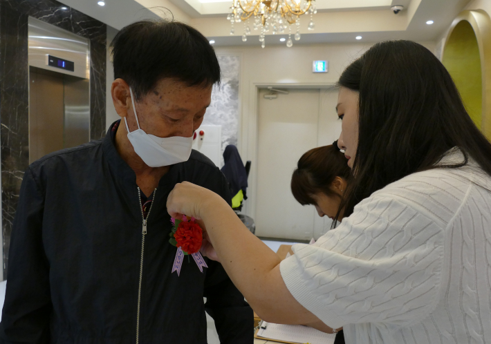 생신 잔치에 참여한 어르신에게 카네이션을 달아드리고 있다.