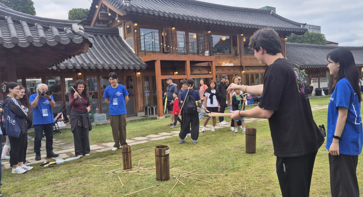 파랑색 상의 단체복을 입은 세 명의 글링이가 투호놀이에서 외국인과 함께 하고 있다.