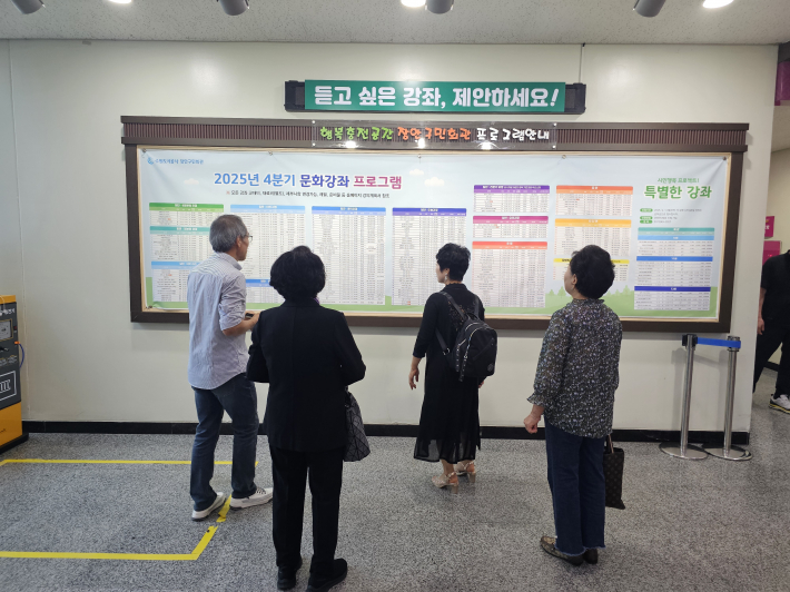 '듣고 싶은 강좌, 행복충전 공간 구민회관 프로그램' 안내판 앞에서 수강 종목을 찾고 있는 시민들