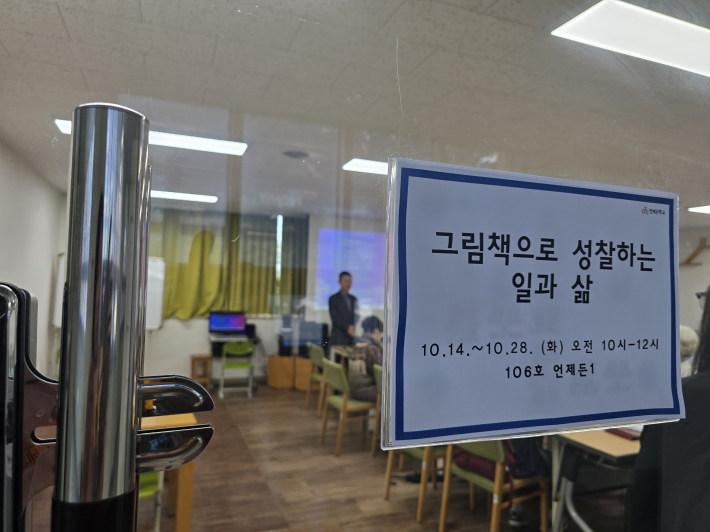 수원시 평생학습관 106호 강의실에 부착된 「그림책으로 성장하는 일과 삶」 안내문 너머로 강의에 집중하는 강사와 수강생들의 모습이 보인다.