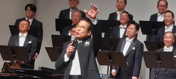 송 지휘자가 마이크를 잡았다.  그는 말하기 내용의 핵심을 위트 있게 전달한다.