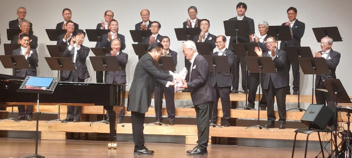 암 투병에서 이겨낸 단원 채영기 장로에게 송 지휘자가 축하 화환을 전달하고 있다.