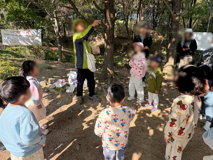 숲해설가 선생님이 단풍나무 열매를 떨어뜨리며 아이들에게 설명하는 모습.