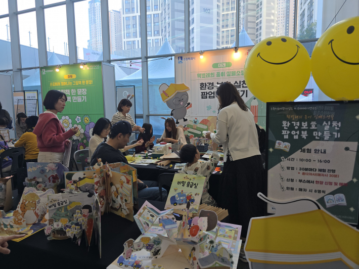 '책벌레의 종이 심폐소생술' 팝업북 만들기 체험  수원시도서관 미래 섹션 부스에서 어린이와 학부모가 함께 환경 보호를 주제로 한 팝업북 만들기에 참여하고 있다.