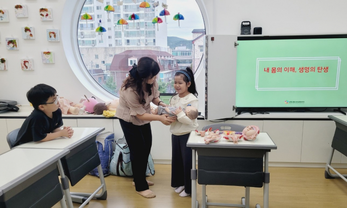 아이들이 아기 교구를 안아보며 생명의 탄생과 부모님에 대한 감사를 느끼는 장면