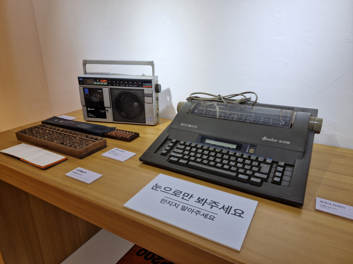 전시 중인 라디오 카세트 플레이어(왼쪽 위), 주판과 케이스(왼쪽 가운데), 금전출납부(왼쪽 아래)와 전자식 타자기(오른쪽) 