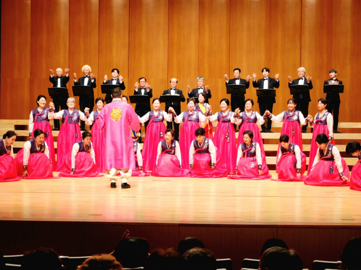 핑크빛 의상을 입은 오현규 지휘자와 시니어합창단원들이 1부를 마치고 인사를 하고 있다.