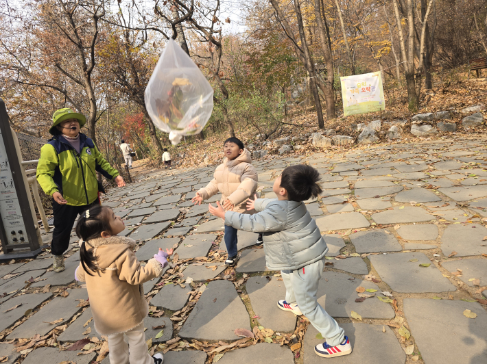 숲 생태해설사와 함께 떨어진 낙엽을 모아 만든 '낙엽 풍선'을 하늘로 띄우며 신나게 뛰어노는 아이들의 모습.