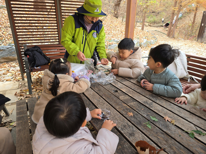 테이블에 둘러앉아 자연물을 활용해 만들기 활동을 하는 아이들과 숲 해설사의 모습.