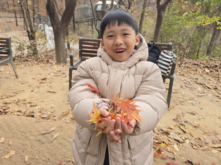 손 가득 모은 알록달록한 단풍잎을 보여주며 즐거워하는 어린이