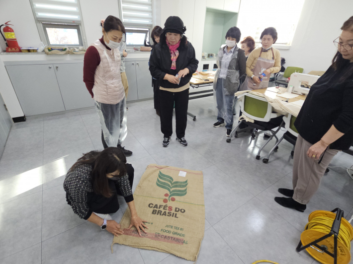 원두 마대를 재단하고 있는 강사와 재단하는 법을 배우는 참가자들