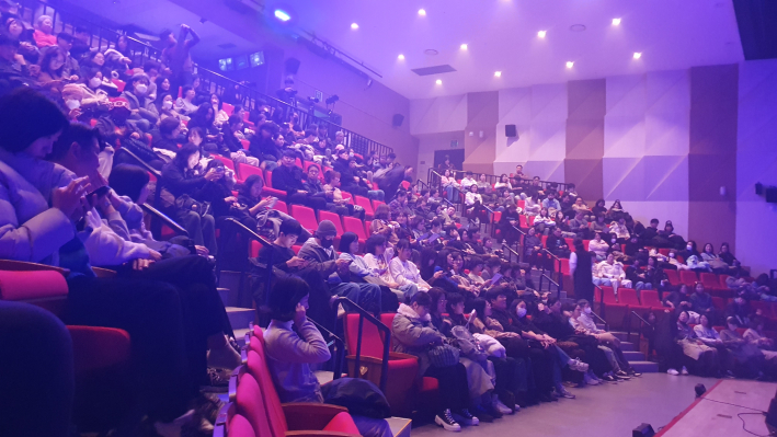 공연 시작 직전, 객석을 가득 메운 관객들이 보랏빛 조명 아래에서 설레는 마음으로 무대를 주시하고 있다.