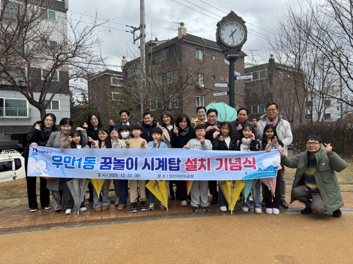 시계탑 앞에서 우만초등학교 어린이, 주민 등이 함께 기념촬영을 하고 있다.