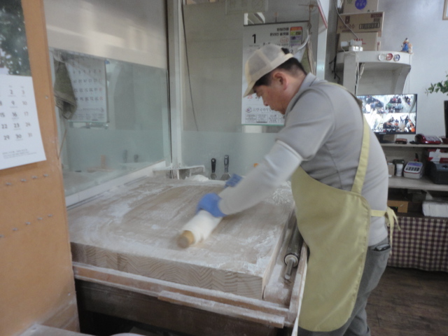 둥굴대로 밀가루 반죽을 엷게 굴리고있다