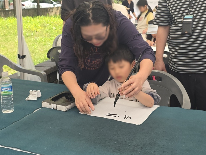 지도 선생님의 손길을 따라 붓을 잡은 아이가 생애 첫 서예에 도전하고 있다.