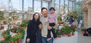 설 연휴를 맞아 수목원 온실을 찾은 4인 가족 관람객이 활짝 핀 제라늄을 배경으로 밝게 미소 지으며 기념사진을 찍고 있는 모습