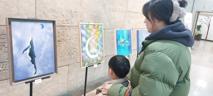 도서관 방문 모자가 전시회 작품을 감상하고 있다.