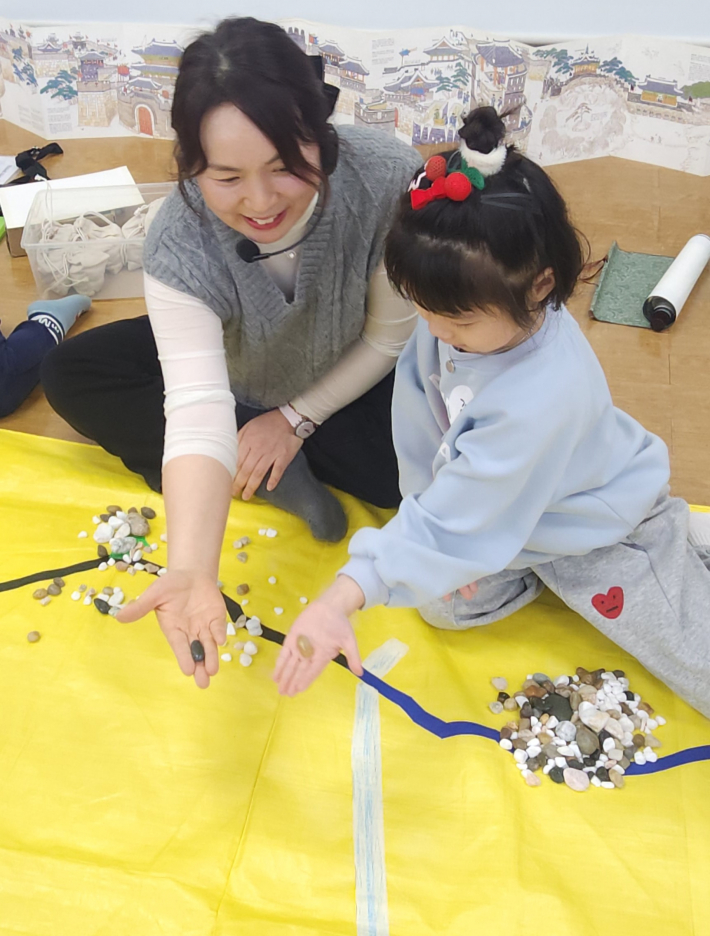 길쭉한 돌을 찾았다며 손을 내민 유아의 발견에 공감하며 놀이를 이어가는 전애희 강사