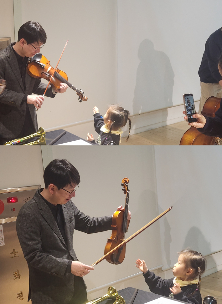 바이올린을 연주하는 단원을 바라보며 손을 뻗는 아이