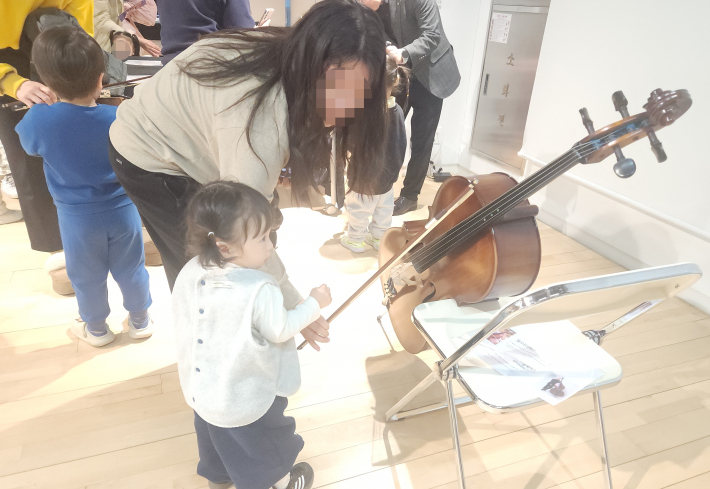첼로 옆에 서서 악기를 바라보는 아이